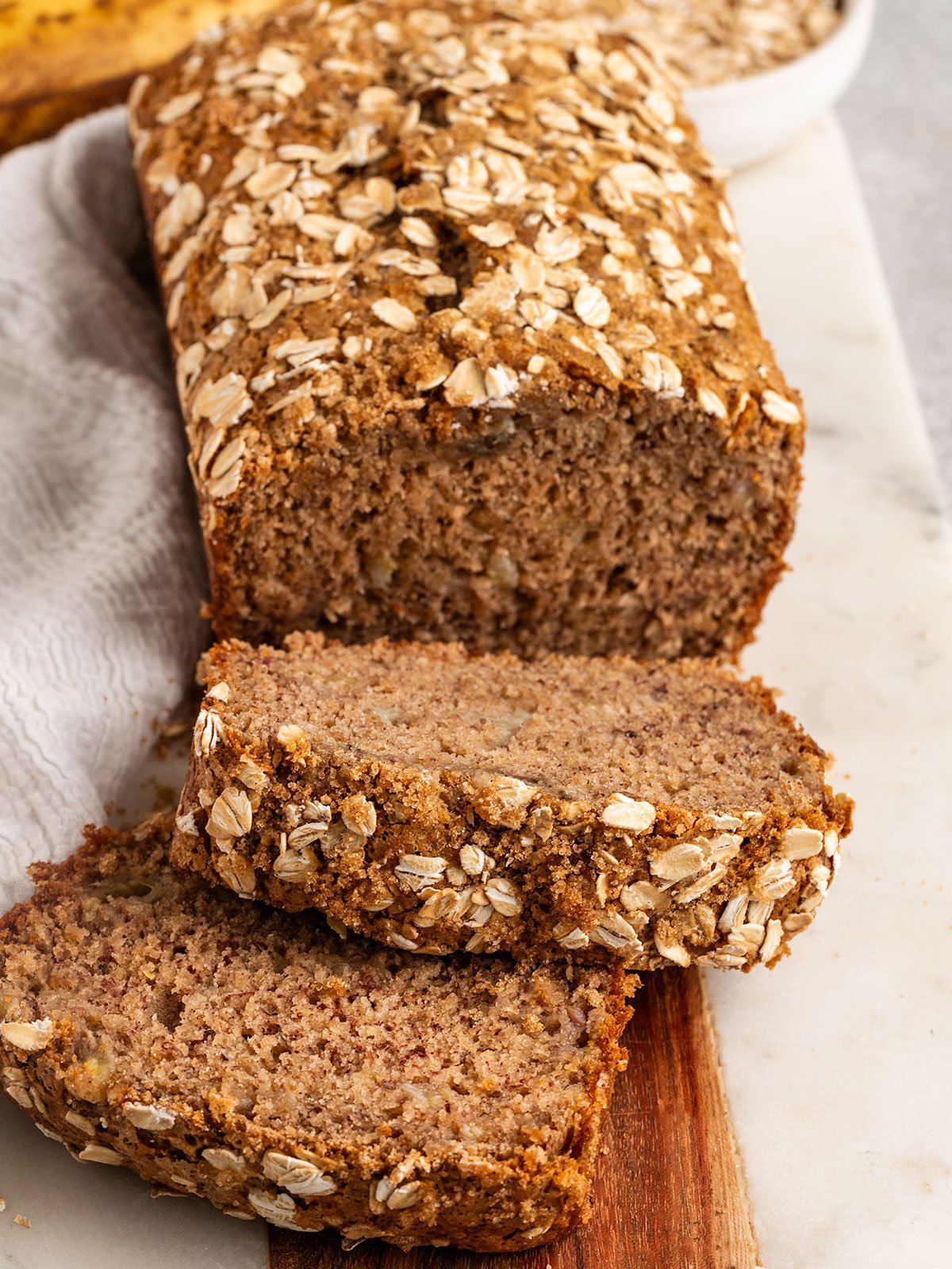 loaf of banana bread topped with oats with two slices cut out.