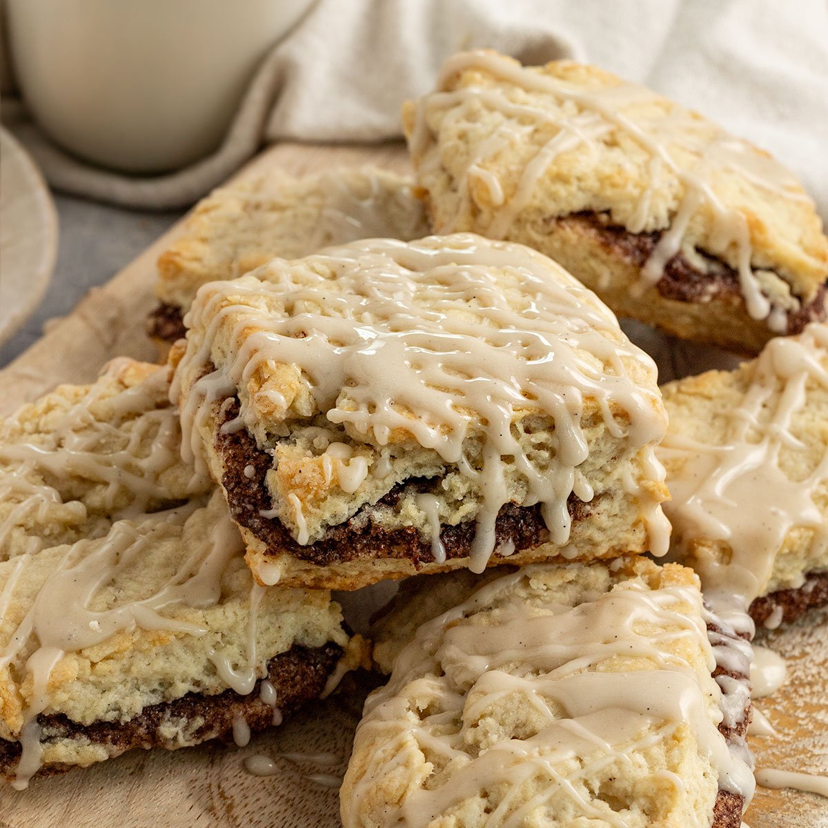 plate of cinnamon sugar filled scones with vanilla icing and a glass of oat milk.