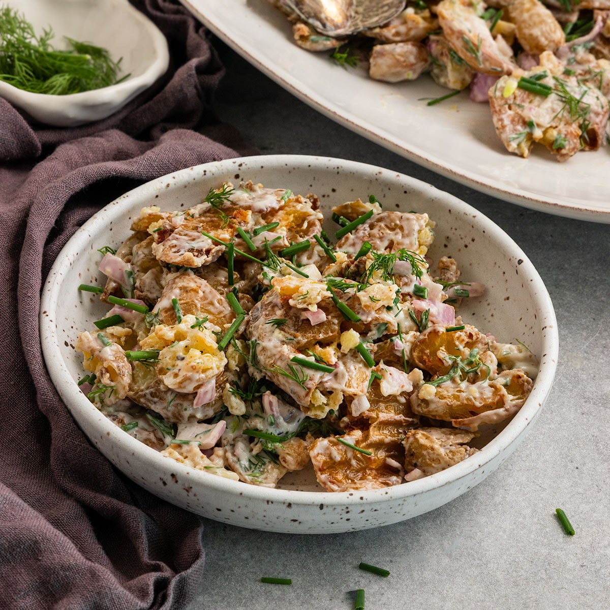 bowl of potato salad with crispy potatoes, chives, dill, and shallots alongside platter of potato salad.