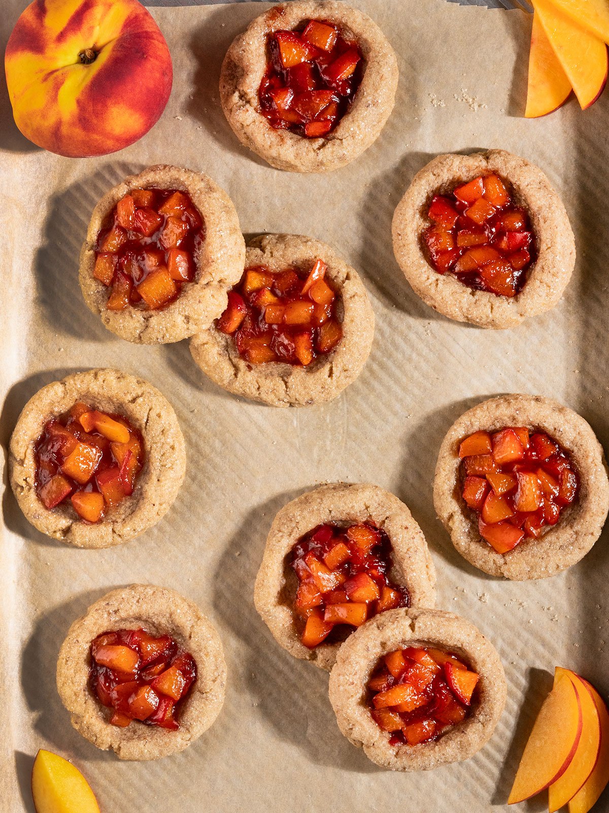 cookies filled with peach filling on a baking tray with fresh peach slices.