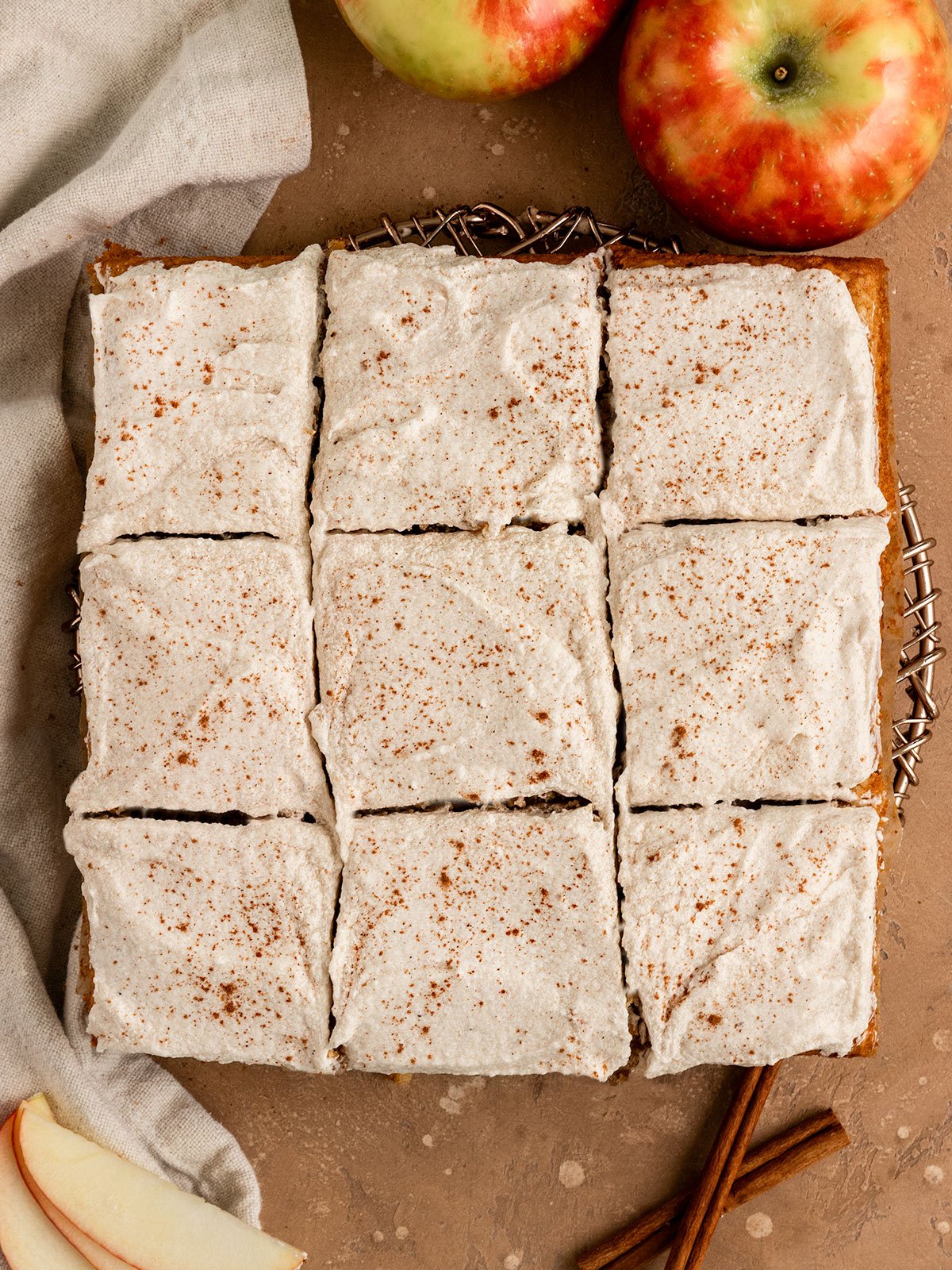 overhead view of apple cake with cinnamon frosting surrounded by fresh apples and cinnamon sticks.