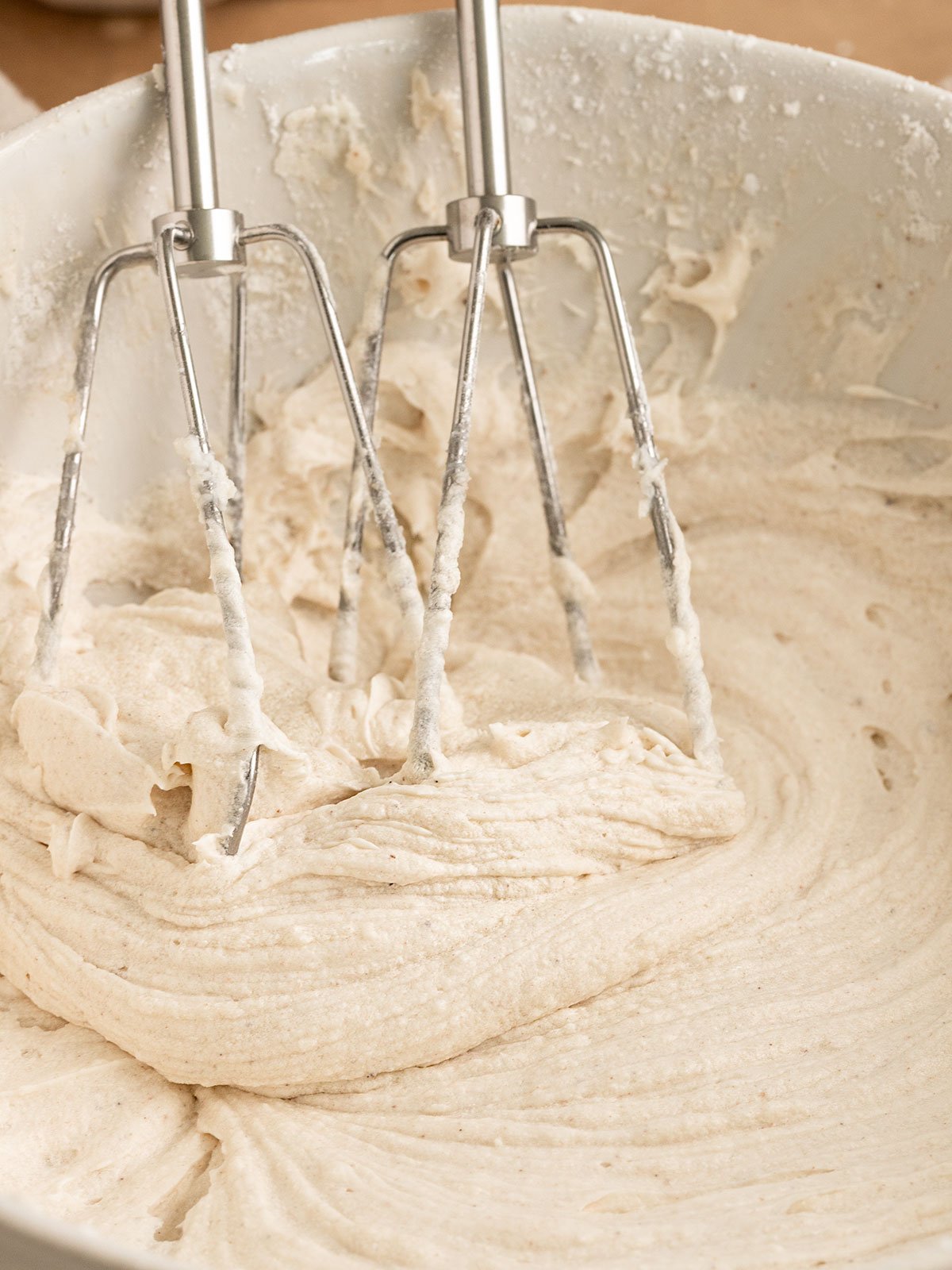 whipped cream cheese frosting in a bowl with electric mixing spoons.