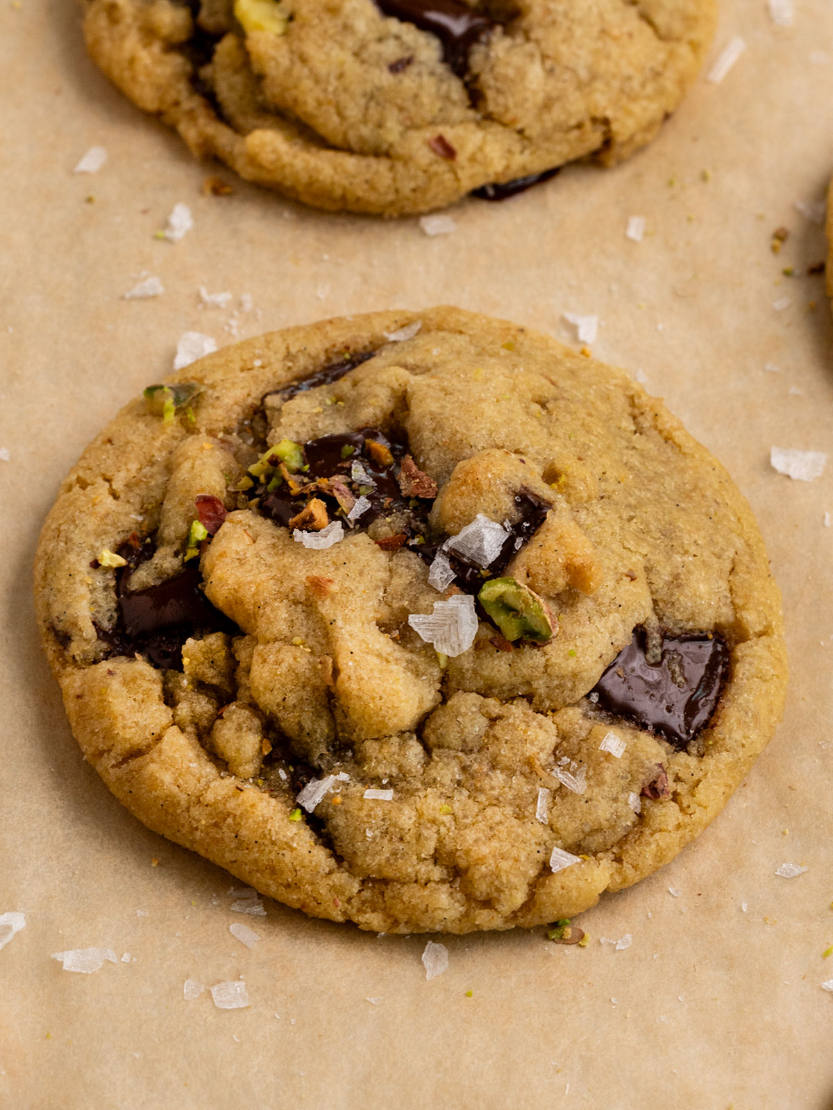 cookie with pistachios, chocolate chunks, and flaky sea salt on a parchment lined baking tray.