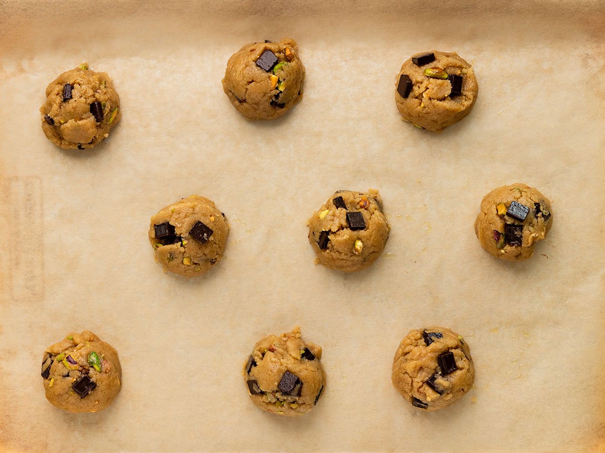 cookie dough balls with pistachios and chocolate chunks on a parchment lined baking tray.