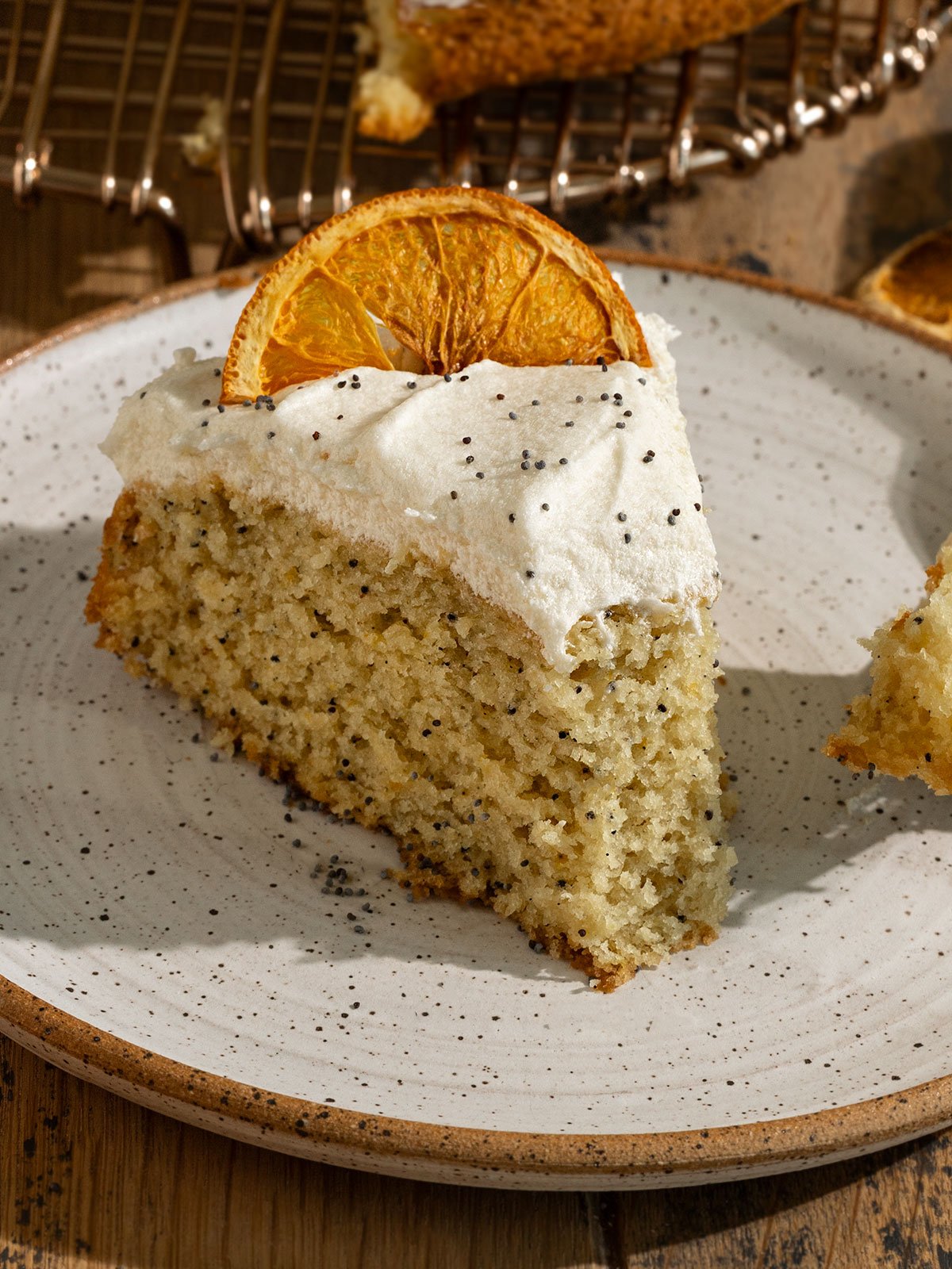 slice of orange poppyseed cake on a plate with frosting and dried orange slice on top.