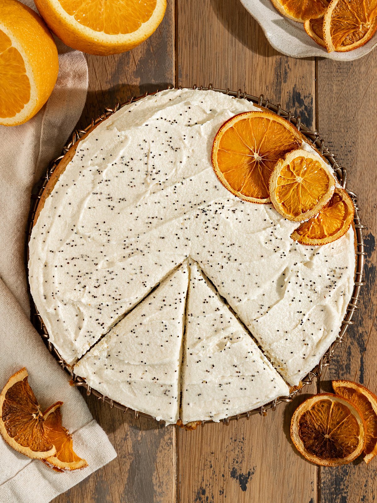 orange poppyseed cake with cream cheese frosting, dried oranges, and poppyseeds on top.