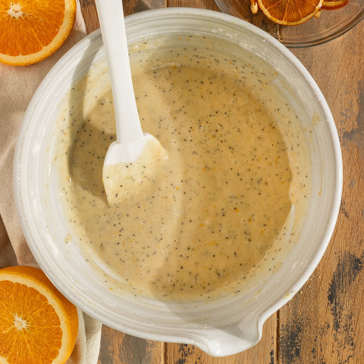 orange poppyseed cake batter in a mixing bowl with spatula.