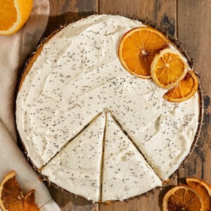 orange poppyseed cake with cream cheese frosting, dried oranges, and poppyseeds on top.