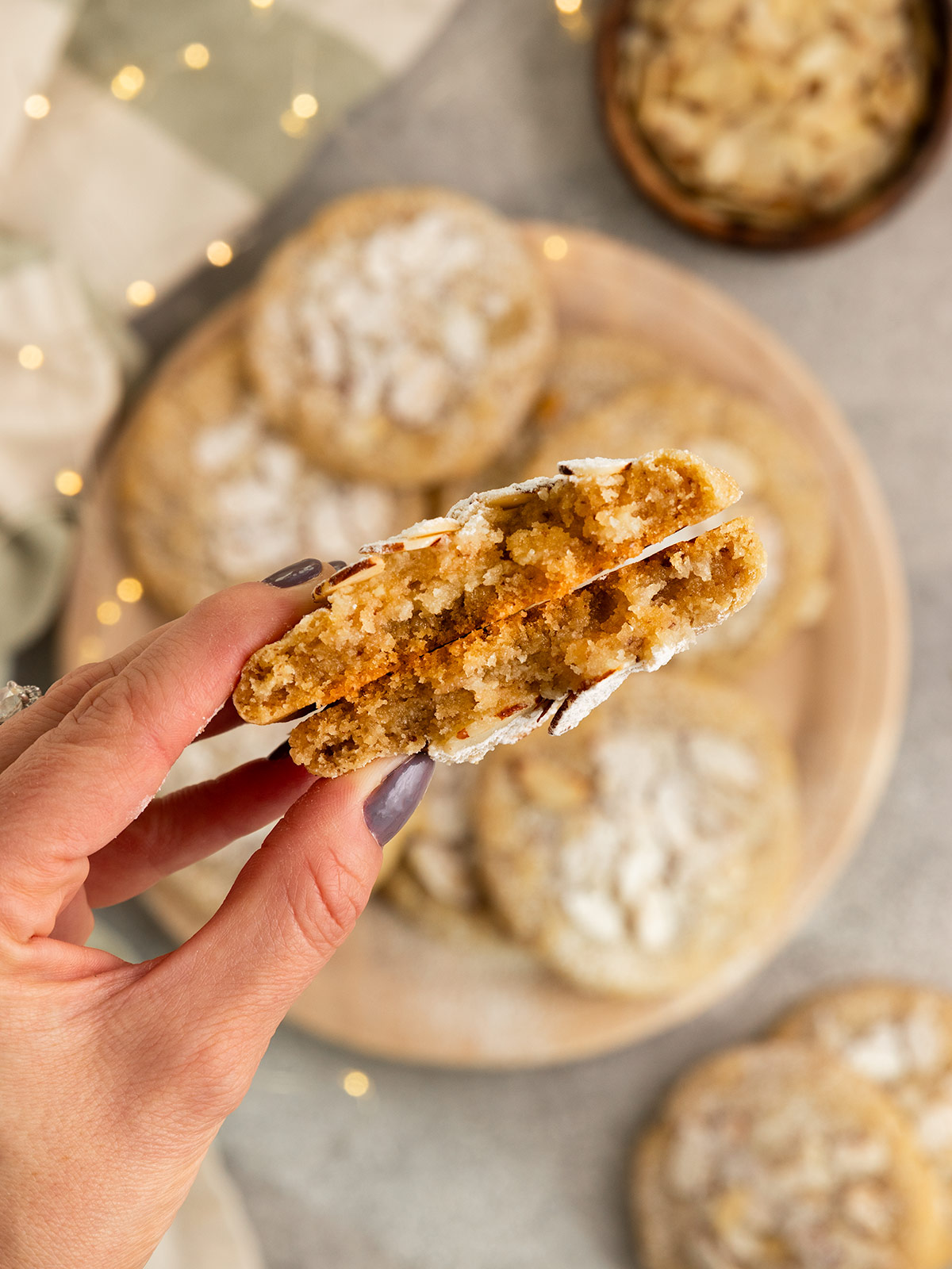 hand holding up almond cookie broken in half to show gooey inside over a plate of cookies.