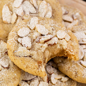 almond cookie with bite taken out stacked on a plate with almond cookies topped with sliced almonds.