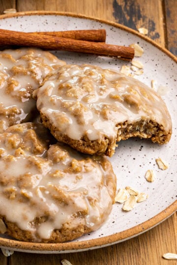 oatmeal cookies with icing on top on a plate with cinnamon sticks.
