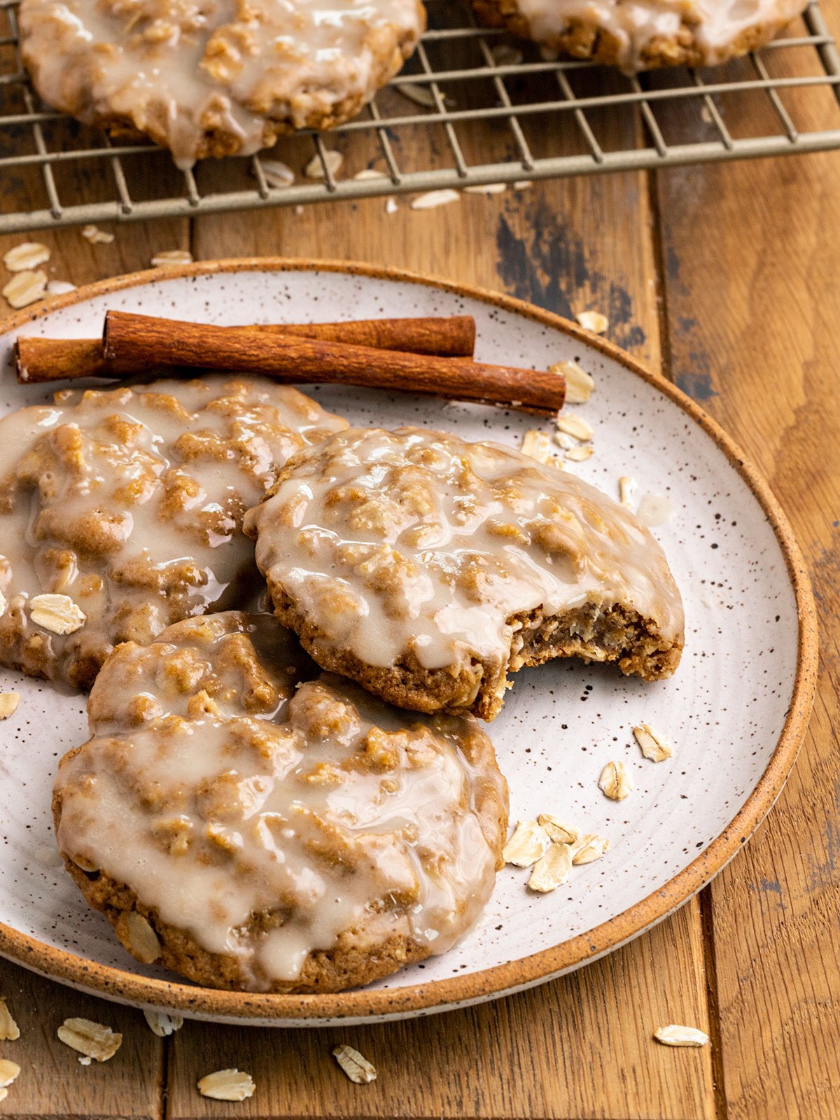 oatmeal cookies with icing on top on a plate with cinnamon sticks.