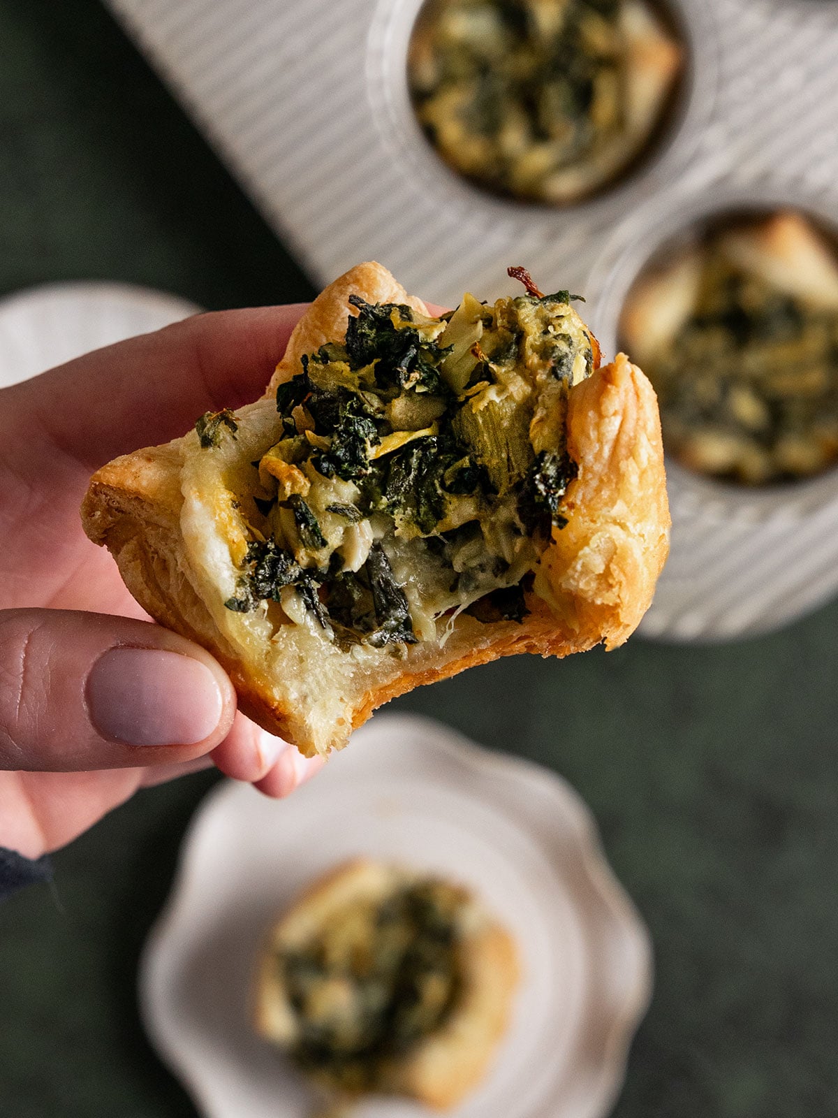 hand holding a bitten puff pastry with spinach artichoke cream filling.