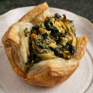 cooked puffed pastry filled with spinach artichoke filling on a plate.