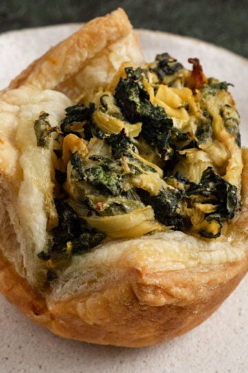 cooked puffed pastry filled with spinach artichoke filling on a plate.