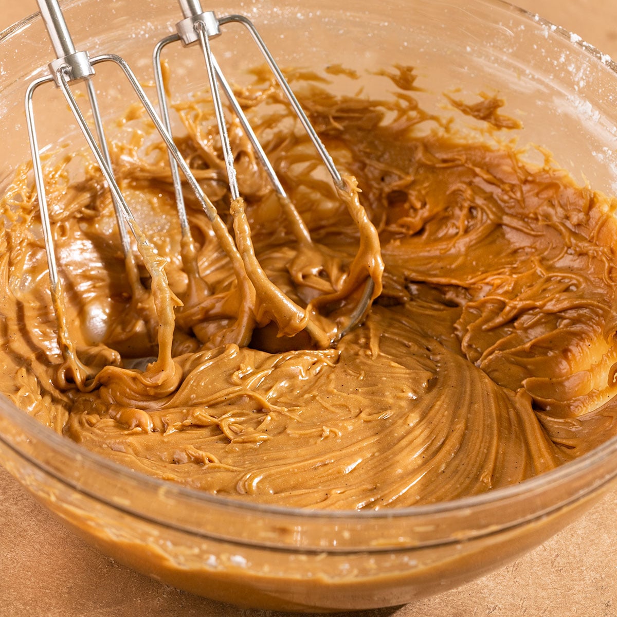 bowl of whipped brown sugar frosting in a glass bowl with beaters.