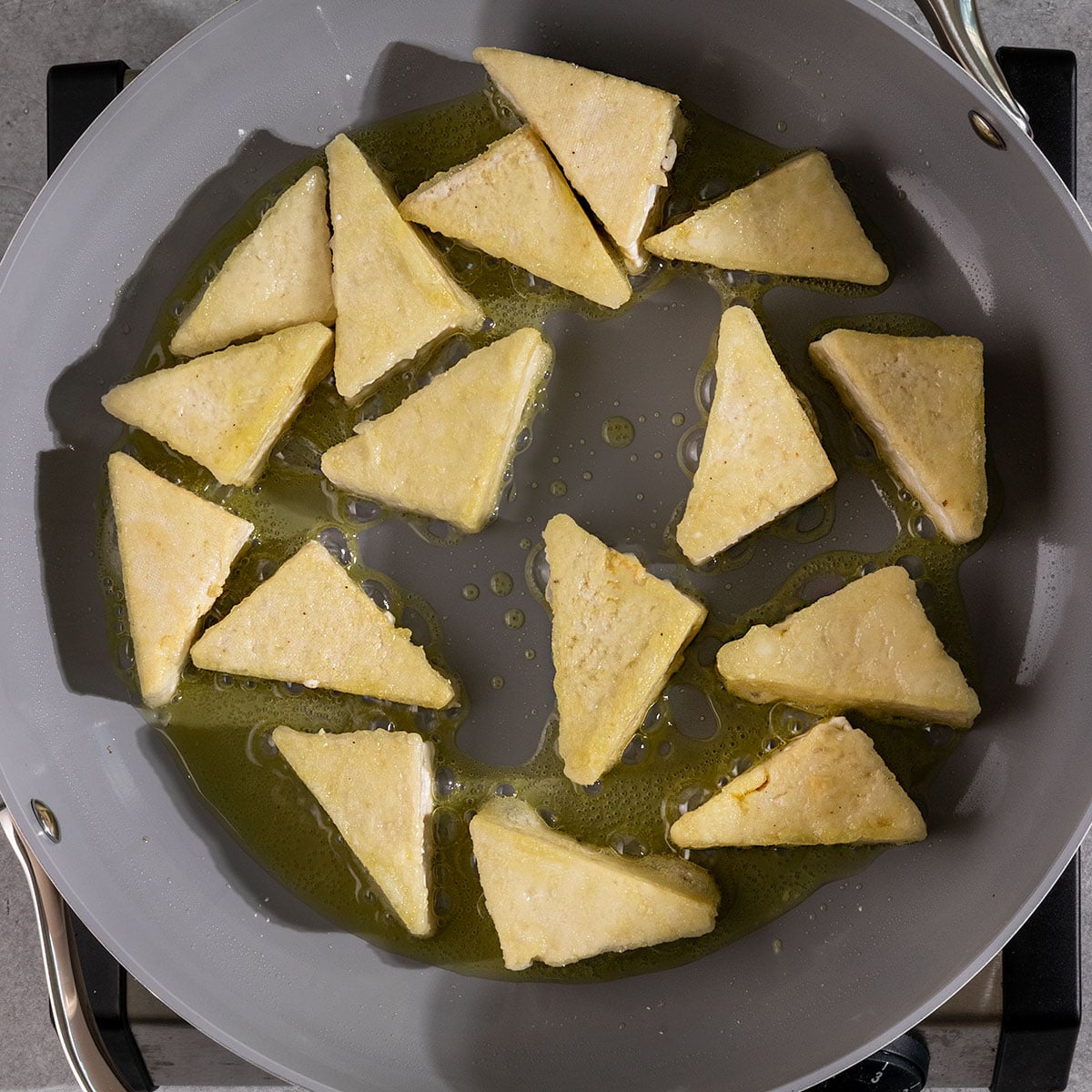 crispy tofu being cooked in pan with oil.