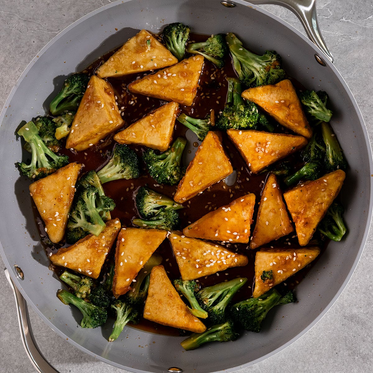 pan with tofu triangles, broccoli, and teriyaki sauce with sesame seeds on top.