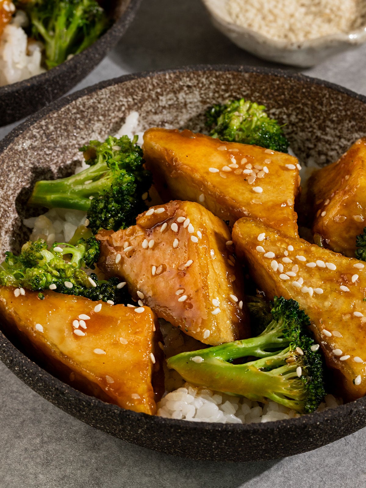 bowl filled with white rice, broccoli, and tofu in a brown teriyaki sauce and sesame seeds on top.
