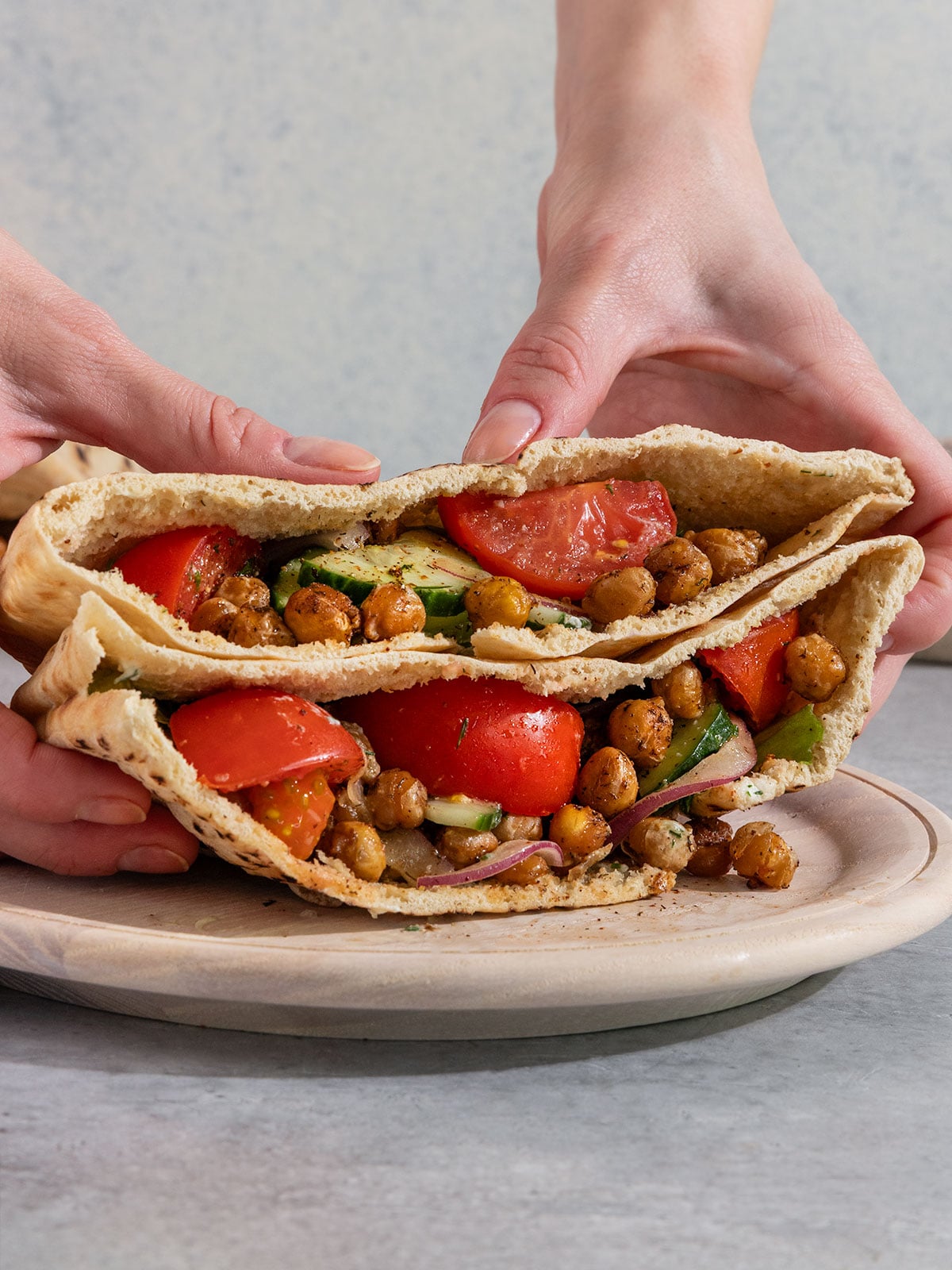 hands holding two pita pockets filled with lettuce, tomato, onion, red onion, and crispy chickpeas.