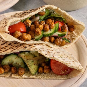 two pita pockets on a plate stuffed with crispy chickpeas, lettuce, tomato, onion, and cucumber.