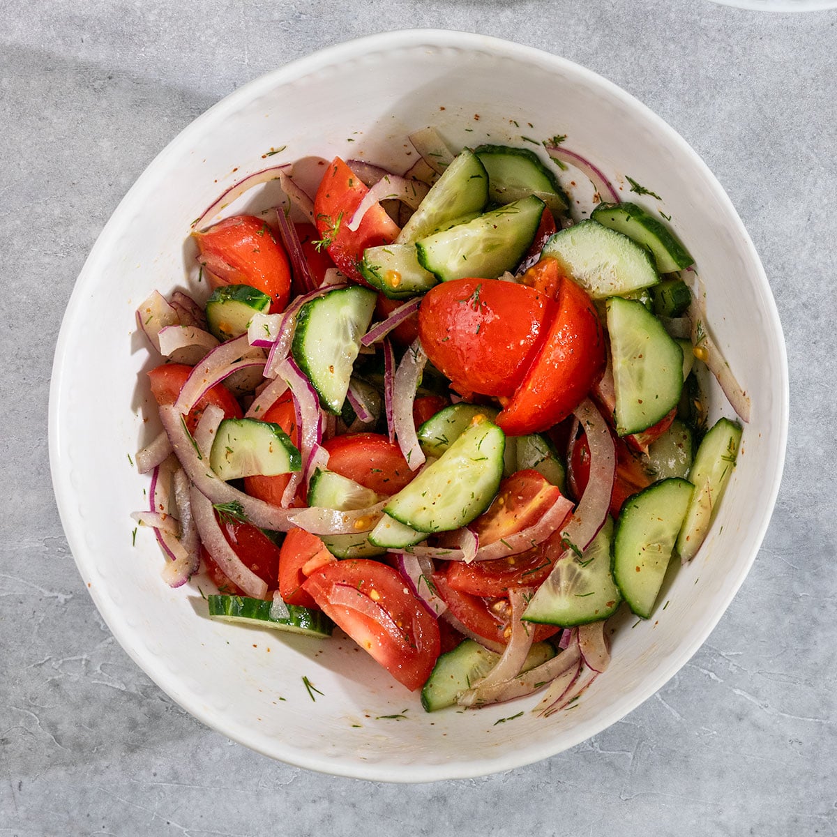 bowl of diced tomatoes, sliced red onions, and sliced cucumber wedges with a dill vinaigrette.