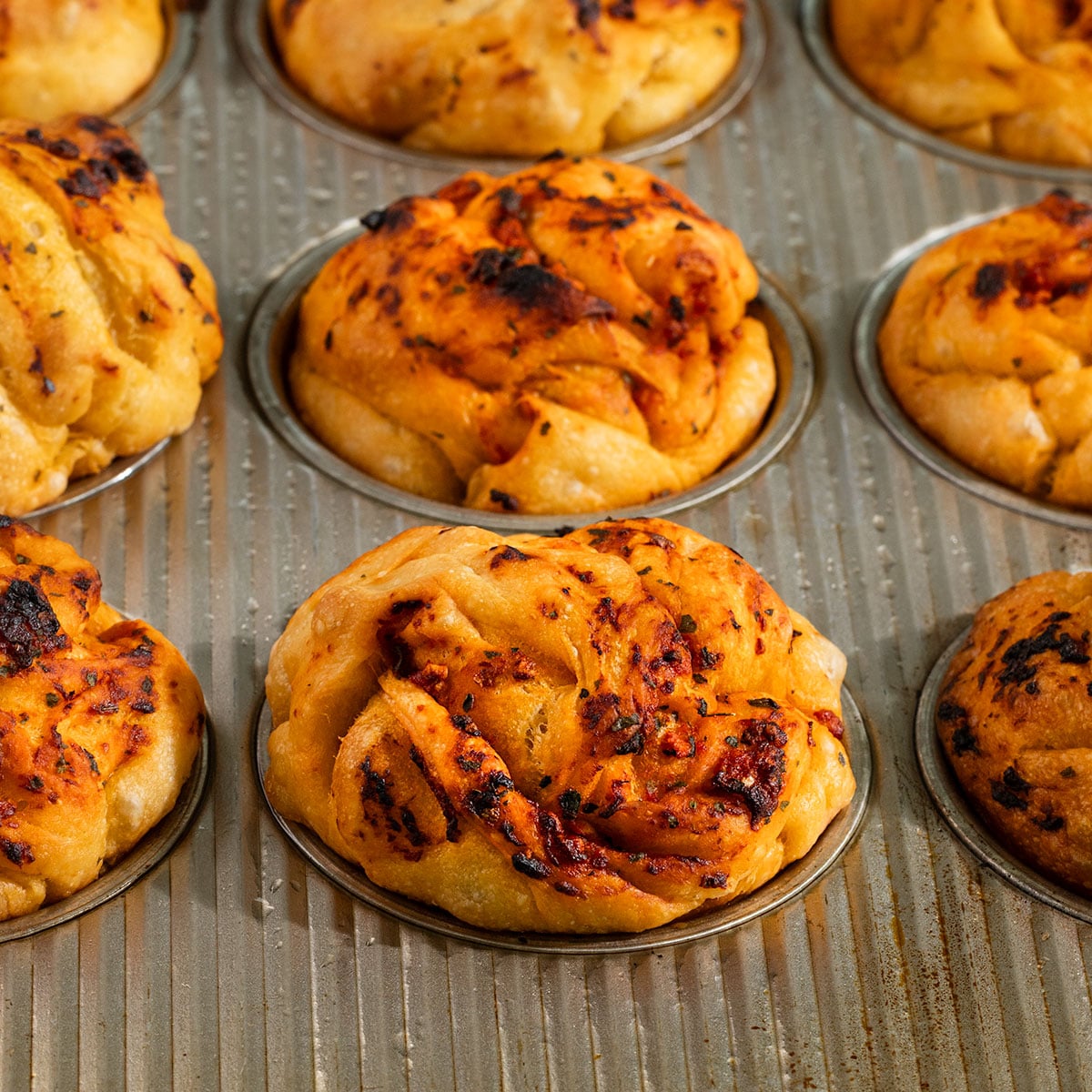 baked focaccia bread muffins topped with tomato and garlic oil in a muffin tin.
