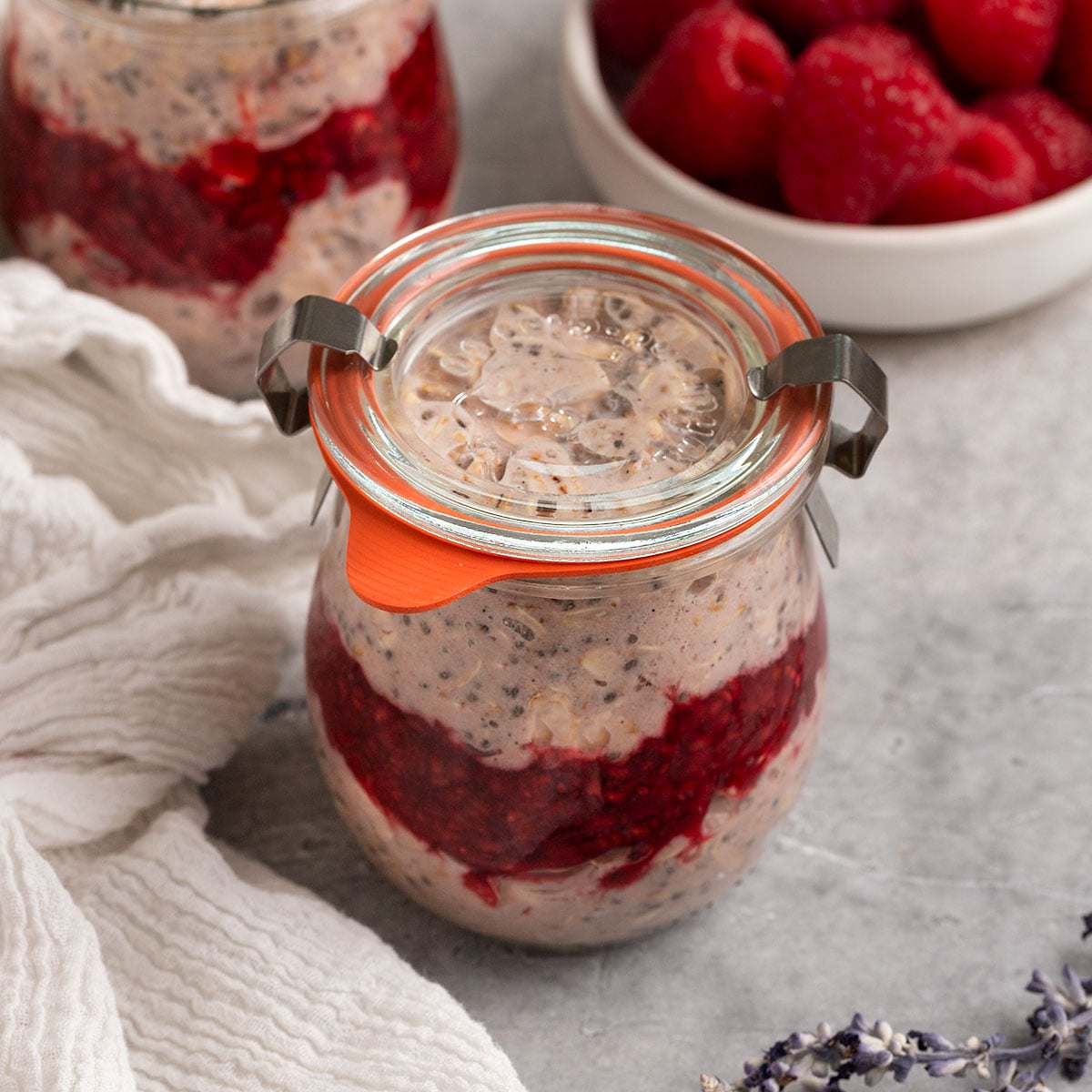 two jars of oats layered with raspberry jam and lids on top.