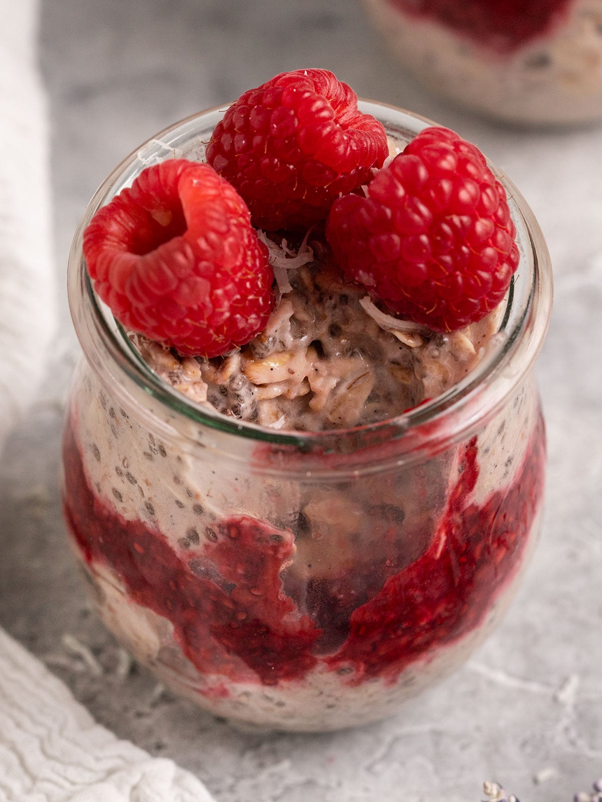 jar of overnight oats with raspberry jam and fresh raspberries with a bite taken out.