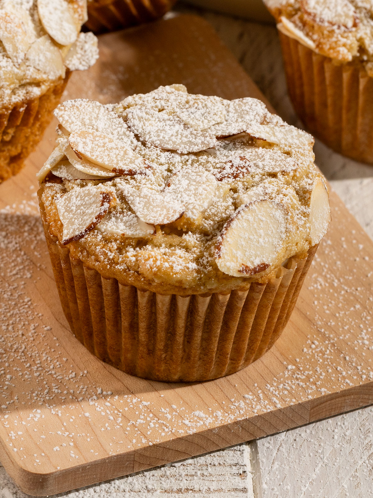 muffin on plate topped with sliced almonds and powdered sugar.