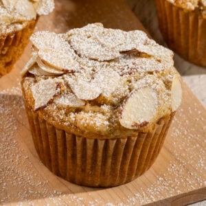 muffin on plate topped with sliced almonds and powdered sugar.