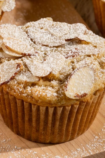 muffin on plate topped with sliced almonds and powdered sugar.