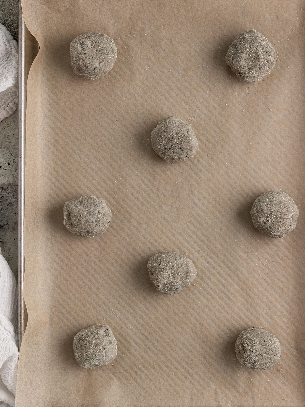 eight sugar coated black sesame cookie dough balls on a parchment lined baking sheet.