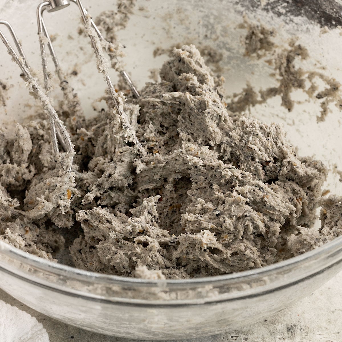 glass bowl full of black sesame cookie dough with mixer paddles in them.