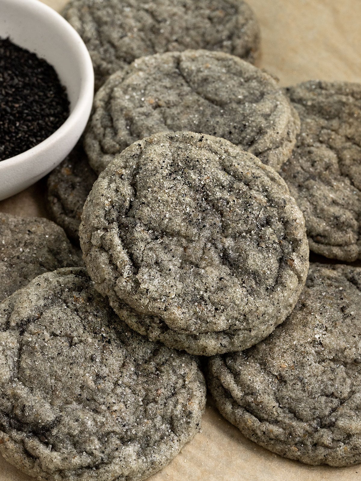 stacked sugar coated black sesame cookies on tray with a small bowl of ground black sesame seeds beside them.