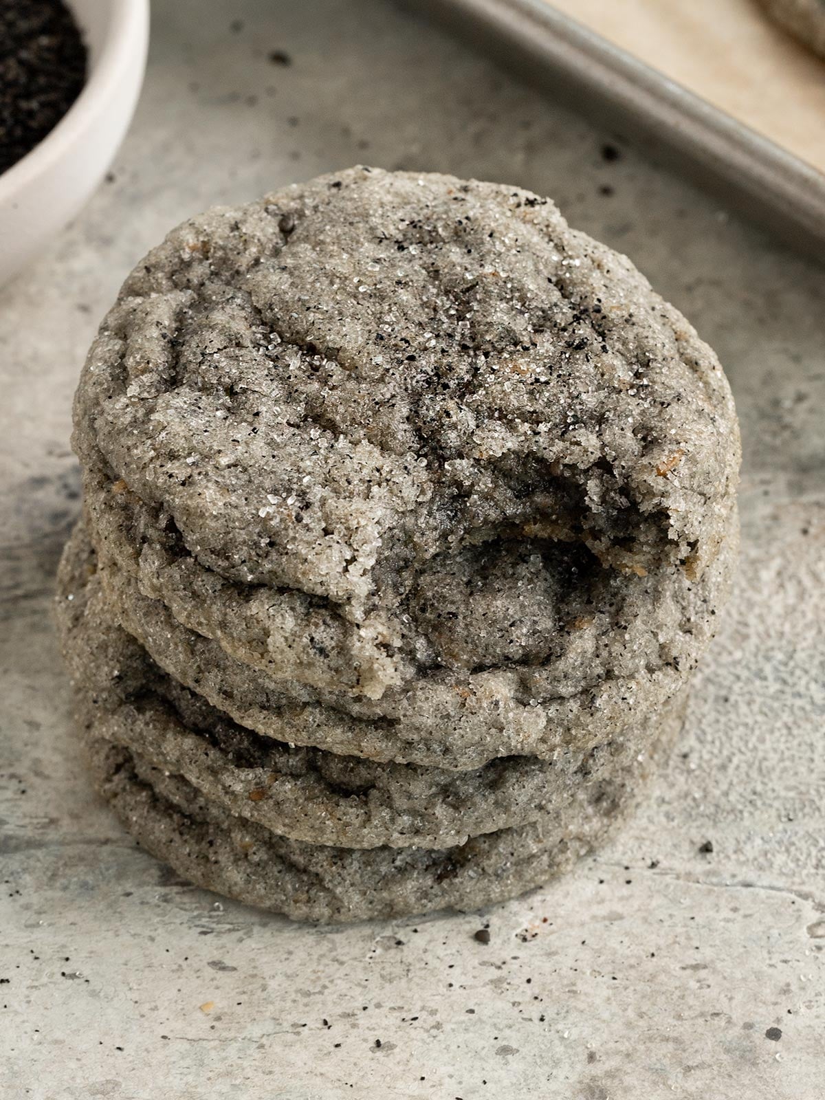 four black sesame sugar cookies stacked on top of each other, top cookie has a bite taken out to show chewy texture inside.