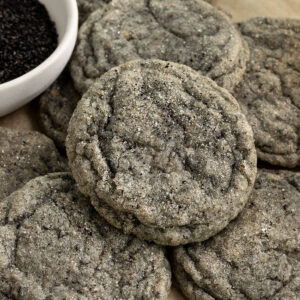 stacked sugar coated black sesame cookies on tray with a small bowl of ground black sesame seeds beside them.