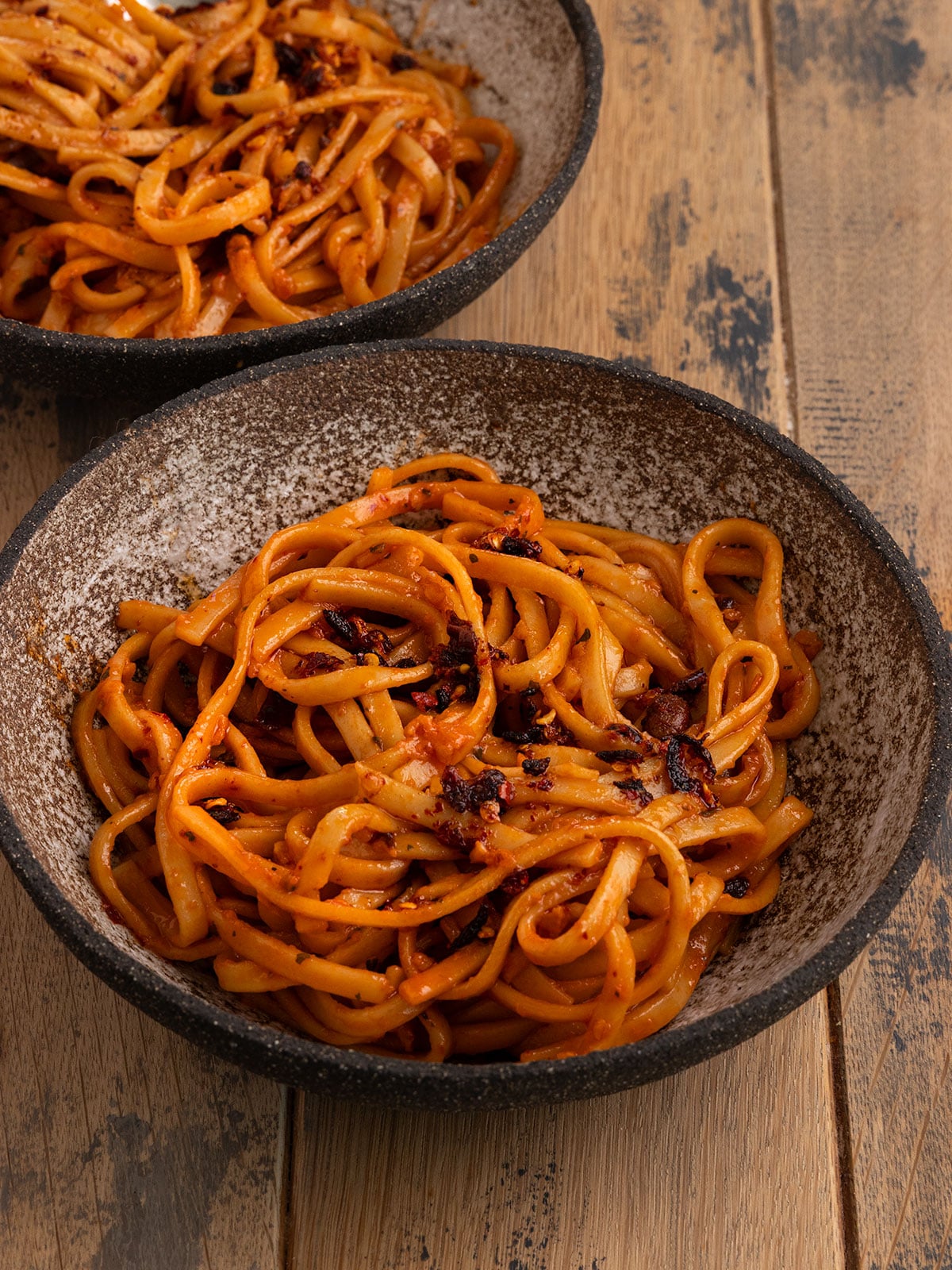 two bowls of noodles topped with a red orange chili garlic sauce and more chili crisp on top.