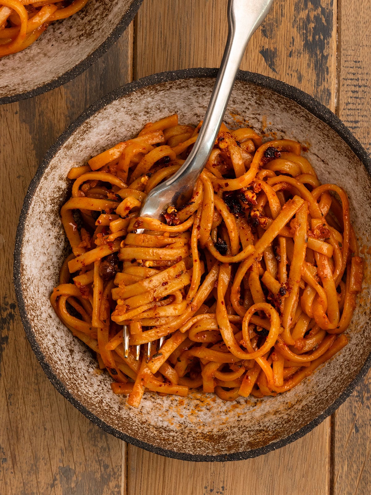 bowl of orange red noodles topped with chili oil and some noodles swirled in a fork.