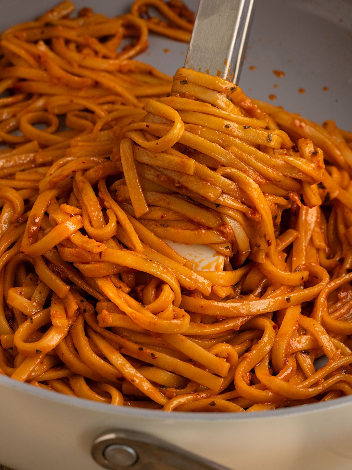 tongs twirling around pasta in a sauce pan.