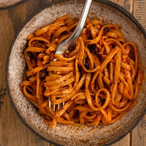 bowl of orange red noodles topped with chili oil and some noodles swirled in a fork.