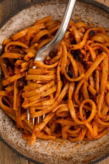 bowl of orange red noodles topped with chili oil and some noodles swirled in a fork.