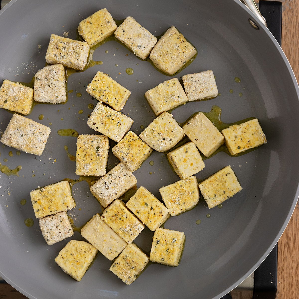 tofu cubes with seasoning on them cooking in a pan with oil.