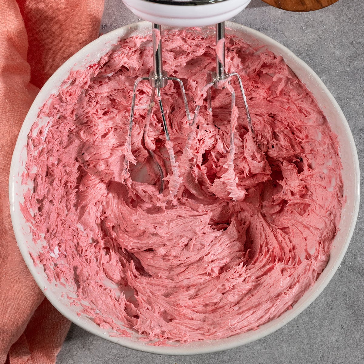 bowl of whipped raspberry frosting with mixer paddle in it.