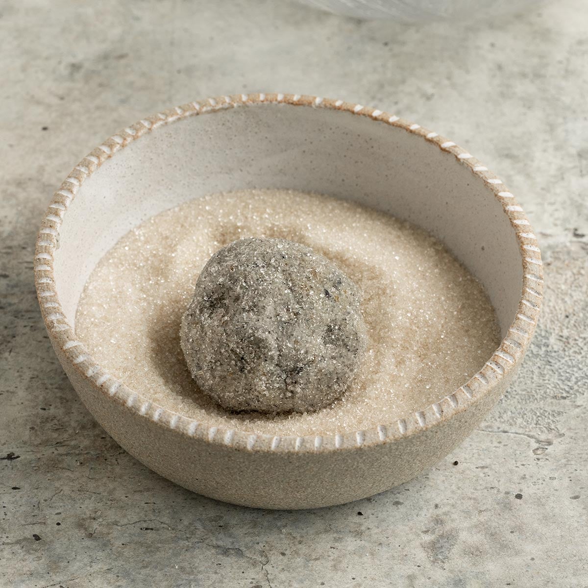 black sesame cookie dough ball coated in sugar in a bowl of sugar.