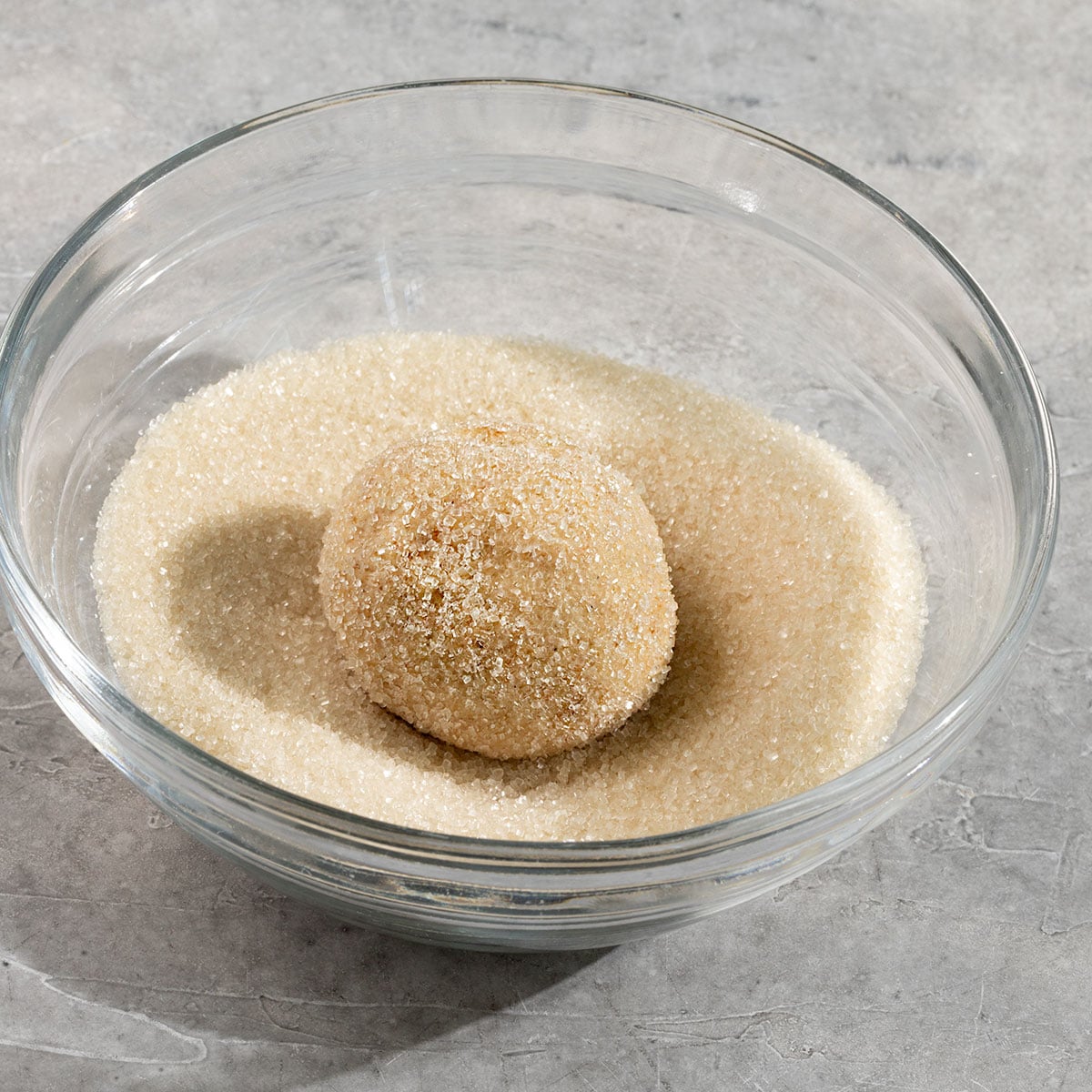 bowl of sugar with a sugar coated cookie dough ball in it.