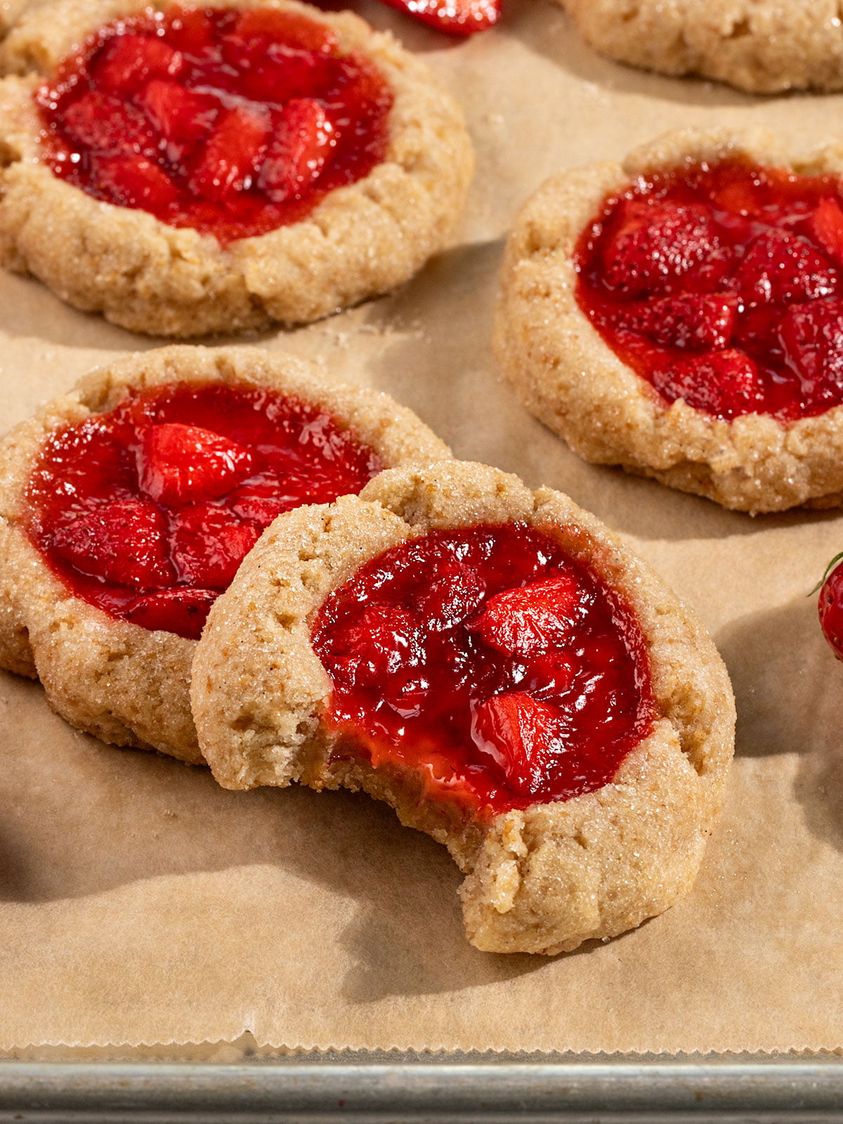tray filled with cookies filled with strawberry jam with the front cookie missing a bite.