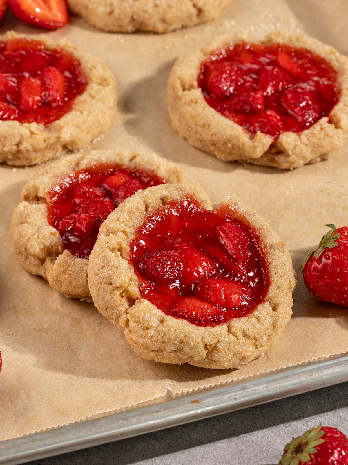 tray of overlapped cookies filled with strawberry jam alongside fresh strawberries.
