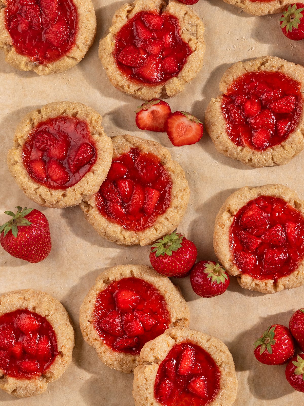 tray of overlapping cookies filled with strawberry jam alongside fresh strawberries.