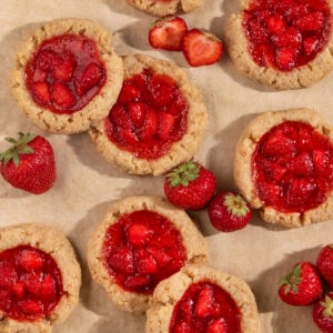 tray of overlapping cookies filled with strawberry jam alongside fresh strawberries.